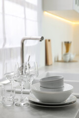 Fototapeta na wymiar Different clean dishware and glasses on countertop near sink in kitchen, space for text