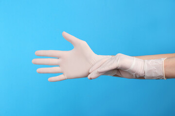 Person putting on medical gloves against light blue background, closeup of hands