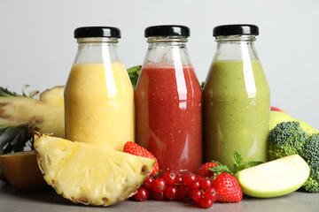 Bottles of delicious juices and fresh fruits on grey table