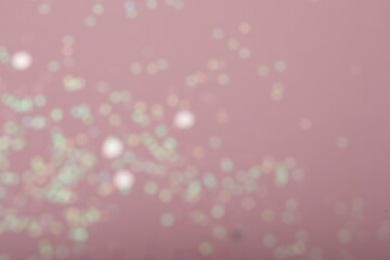 Blurred view of white glitter on pink background. Bokeh effect