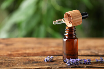 Obraz na płótnie Canvas Bottle of lavender essential oil and flowers on wooden table against blurred background. Space for text