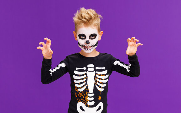 Happy cheerful boy in skeleton costume  celebrates Halloween and scary gesture  on purple background