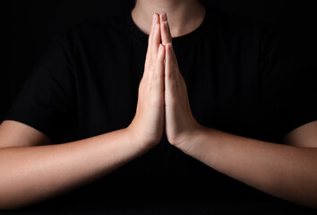 Woman holding hands clasped while praying against black background, closeup