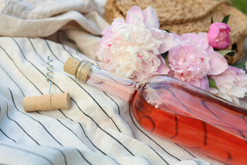 Bottle of rose wine and beautiful peonies on light blanket, closeup