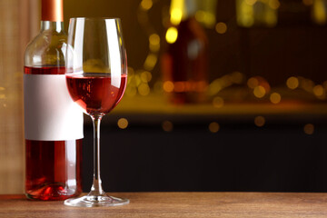 Bottle and glass of delicious rose wine on wooden table in bar. Space for text