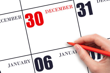 A hand holding a red pen and pointing on the calendar date December 30. Red calendar date, copy space, mockup.