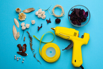 Hot glue gun and handicraft materials on light blue background, flat lay