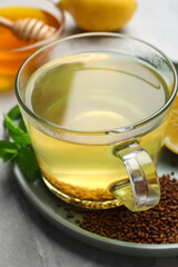 Cup of aromatic buckwheat tea, mint and granules on light grey marble table, closeup