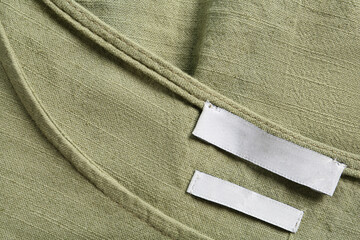 Blank clothing label on green apparel, top view. Space for text
