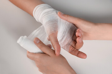 Doctor applying bandage onto patient's hand on white background, top view. Closeup