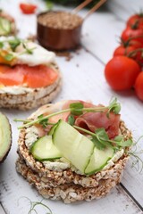 Crunchy buckwheat cakes with cream cheese, prosciutto and cucumber slice on white wooden table, closeup
