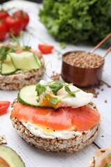 Crunchy buckwheat cakes with salmon, poached egg and microgreens on white wooden table, closeup
