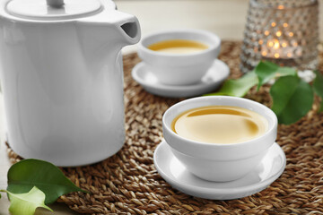 Green tea in white cups with leaves and teapot on table, closeup