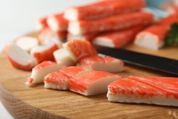 Sliced crab sticks and knife on wooden cutting board, closeup