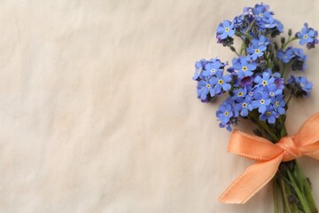 Beautiful blue forget-me-not flowers tied with ribbon on light background, top view. Space for text