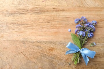 Beautiful blue forget-me-not flowers tied with ribbon on wooden table, top view. Space for text