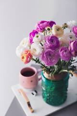 Bouquet of beautiful ranunculuses and tea on table near light grey wall