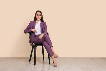 Young businesswoman sitting on chair near beige wall in office, space for text