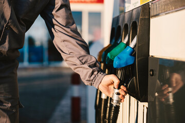 The hands of a gas station worker hold the petrol dispenser.