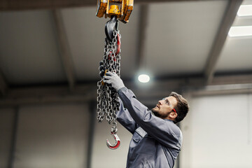 A heavy industry worker hanging chains on an industrial hook in the facility.