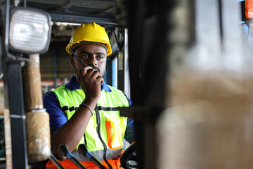 Warehouse workers or forklift driver man with hardhats and reflective jackets in vehicle using walkie talkie radio controlling stock and inventory in retail warehouse logistics, distribution center