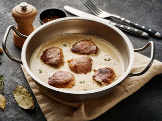 Pork meat medallions with cream sauce in skillet