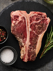 Raw fresh beef T-bone steak with rosemary, salt and pepper.