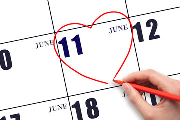 A woman's hand drawing a red heart shape on the calendar date of 11 June. Heart as a symbol of love.