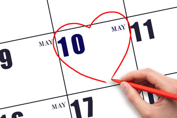 A woman's hand drawing a red heart shape on the calendar date of 10 May. Heart as a symbol of love.