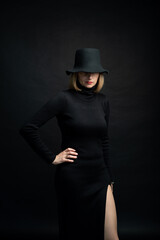 Fototapeta na wymiar blonde woman wearing black slim dress and black hat on dark background