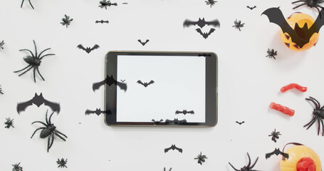 Image of halloween spiders, bats and decorations over tablet on white background
