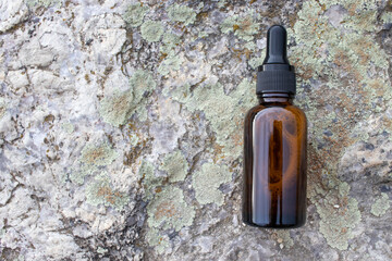 Amber glass dropper bottle of face serum or essential oil on granite stone rock textured background outdoor. Natural organic spa cosmetic concept. Top view, copy space	