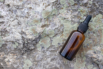 Amber glass dropper bottle of face serum or essential oil on granite stone rock textured background outdoor. Natural organic spa cosmetic concept. Top view, copy space	