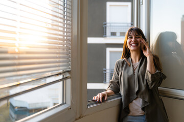 Smiling woman talking on a mobile phone next to a window
