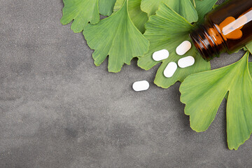 Bottle of pills and fresh ginkgo biloba leaves on grey background. Traditional, herbal medicine and...