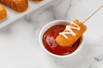Eating Corn dog with ketchup and mayo on white marble background. Traditional American street food. Fried sausage on a stick. Сorn dog, corndog.