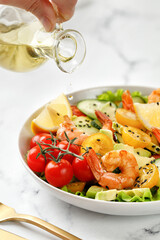 Pouring oil into a salad. Fresh seafood salad with prawns, shrimps, avocado, cucumber on white marble background. Drop or oil. Healthy diet concept.