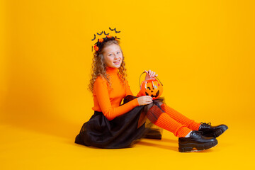 a teenage girl in a witch costume on a yellow background, holding a confent pumpkin eating marmalade worms halloween party