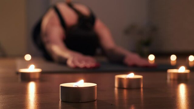 young girl in a black sports uniform practices yoga at home by candlelight