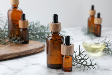Bottles of juniper essential oil and twigs on white marble table