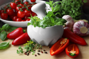 Mortar with fresh herbs near garlic, pepper and cherry tomatoes on wooden table, closeup