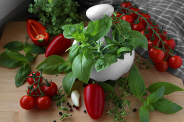 Mortar with fresh herbs, cherry tomatoes and pepper on wooden table