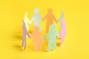 Many different paper human figures standing in circle on yellow background. Diversity and inclusion...