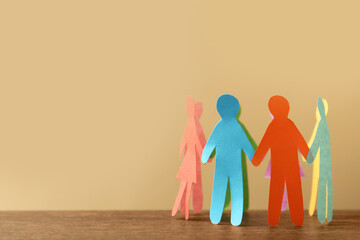 Many different paper human figures standing in circle on wooden table against beige background,...