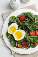 Delicious salad with boiled egg, bacon and tomatoes served on white wooden table, flat lay