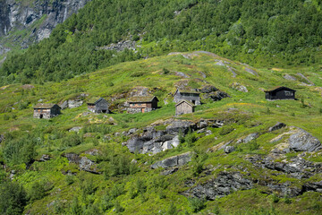 Fototapeta na wymiar Wonderful landscapes in Norway. Vestland. Beautiful scenery of houses with grass roof. Norwegian traditional architecture. Mountains and trees in background. Cloudy day. Selective focus