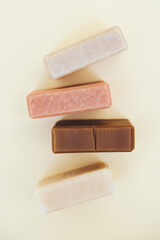 Soap bars made with natural herbal ingredients over light yellow background. Making vegan skincare products and cosmetics at home. Flat lay style, vertical image. View from above