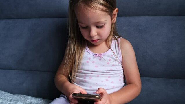 Little Girl Watching Smartphone in Bed Before Going Sleep addicted with gadgets