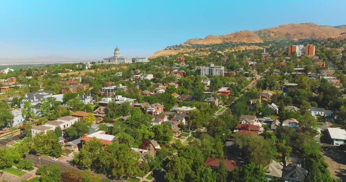 Beautiful sunny city built near the bare mountain. Magnificent State Capitol Building at the foot of rock. Salt Lake City panorama on clear summer day.