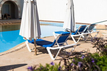 Swimming pool with clean clear water, nobody. Square shaped pool with blue tiles with grab bars ladder and sunbeds on the decks, no people. water surface. Overhead view. Summer background.